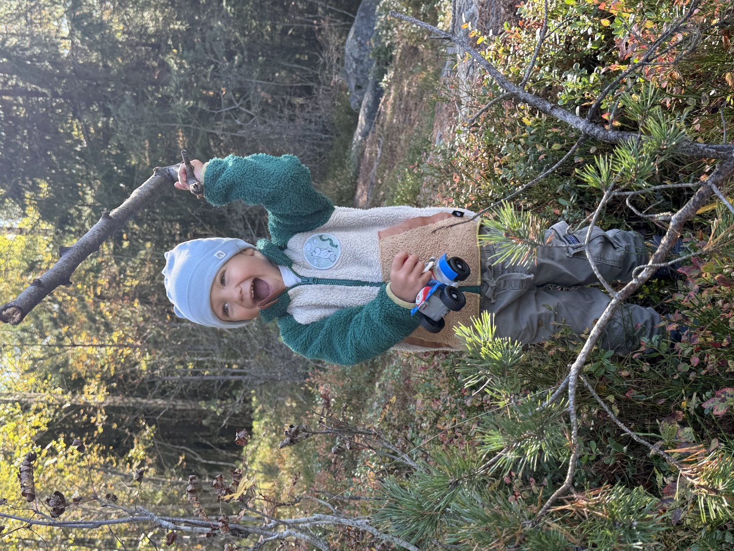 En smilende gutt utforsker skogen med en pinne i hånden